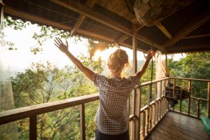 Young woman on a canopy tour adventure in the rain forest in northern Laos looking at the beautiful natural landscape in a sunny summer day. She is on a tree house up in the jungle, arms outstretched for freedom and success.
